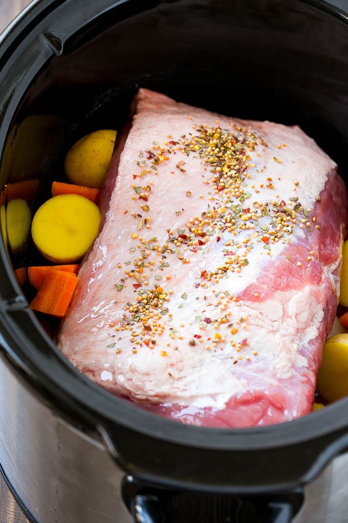 A corned beef roast in a slow cooker with carrots and potatoes.