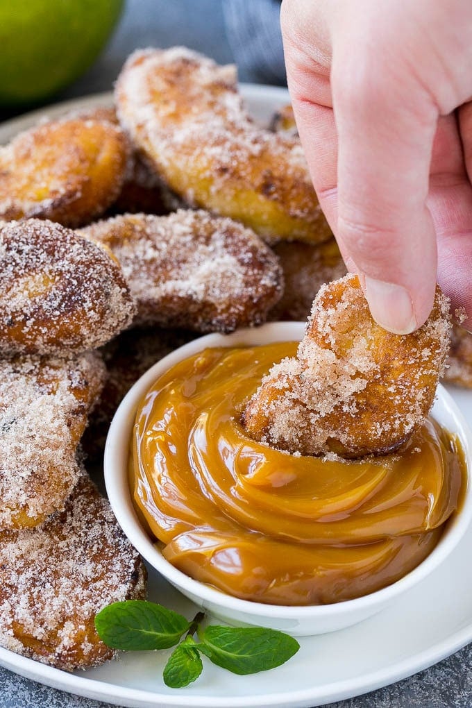 An apple fry being dipped into caramel sauce.