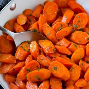 Candied carrots in a pan with a serving spoon.