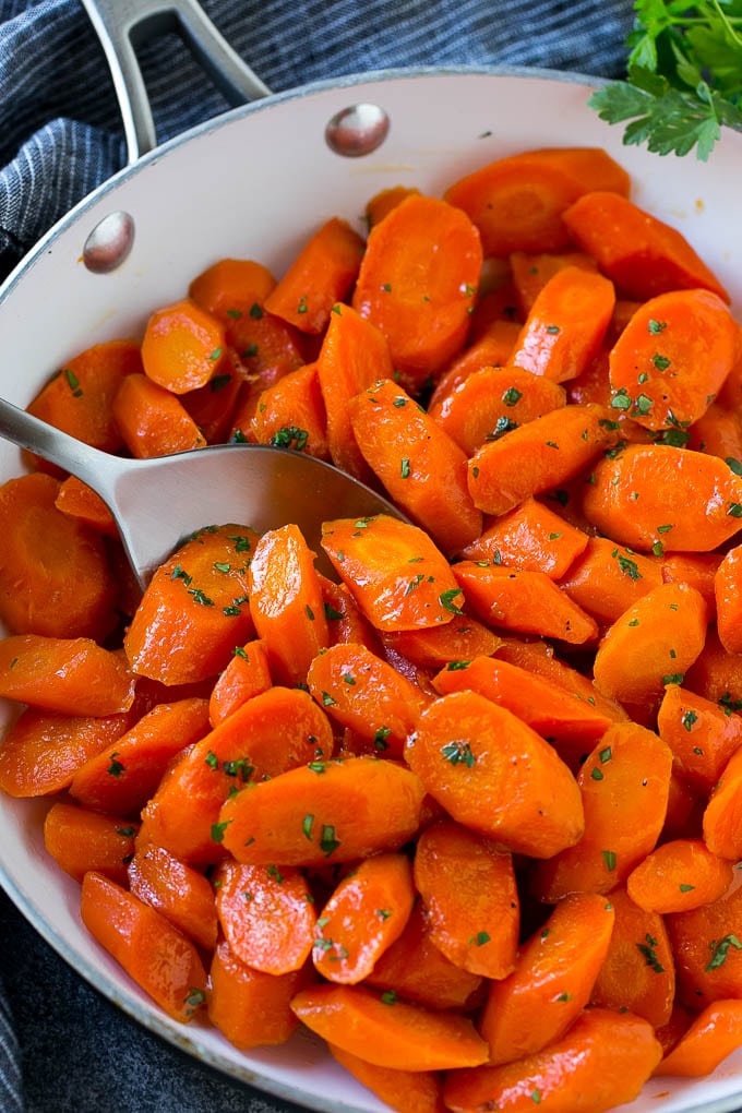 Candied carrots in a pan with a serving spoon.