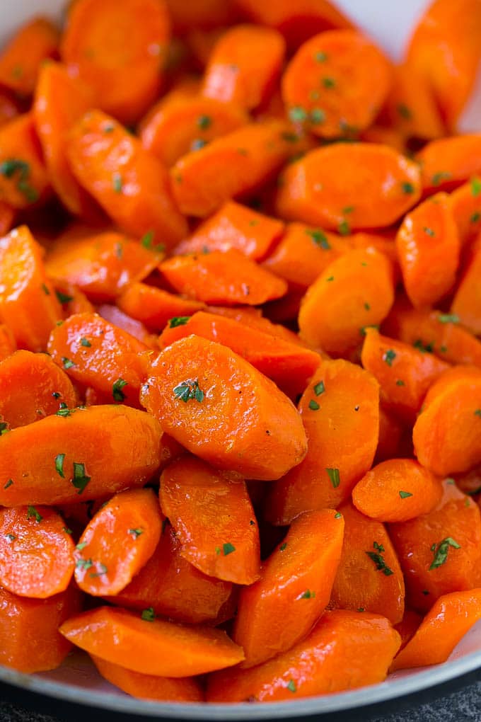 A close up of cooked candied carrots topped with parsley.