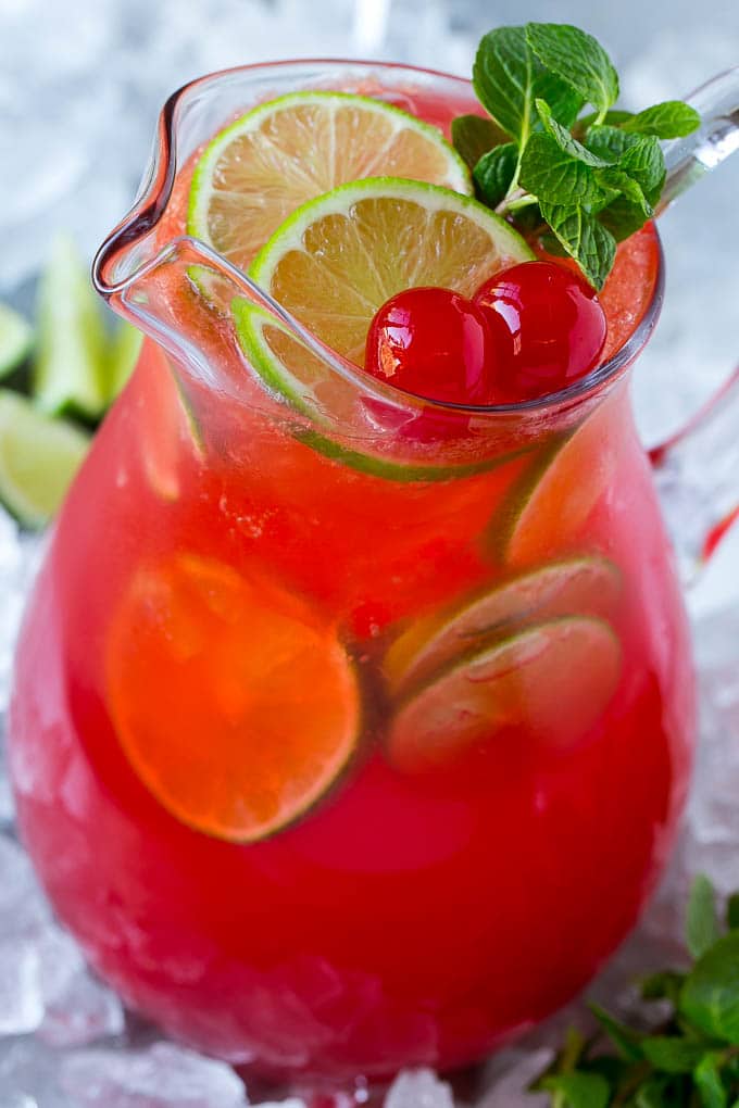 A pitcher of cherry limeade with lime slices, maraschino cherries and mint sprigs.