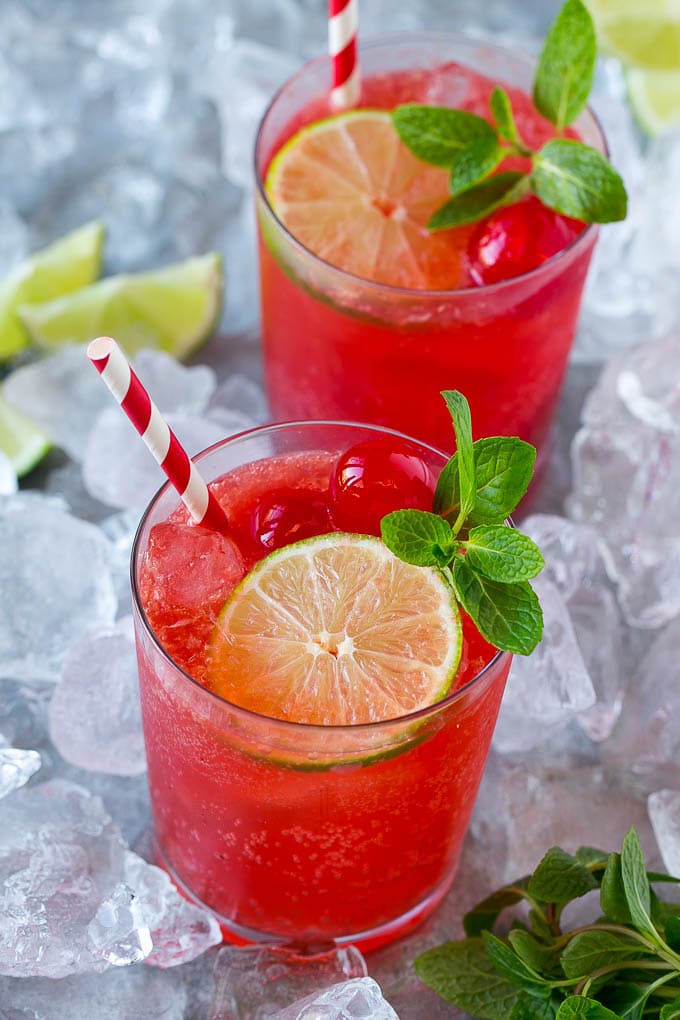 Cups of cherry limeade garnished with mint, lime and cherries.