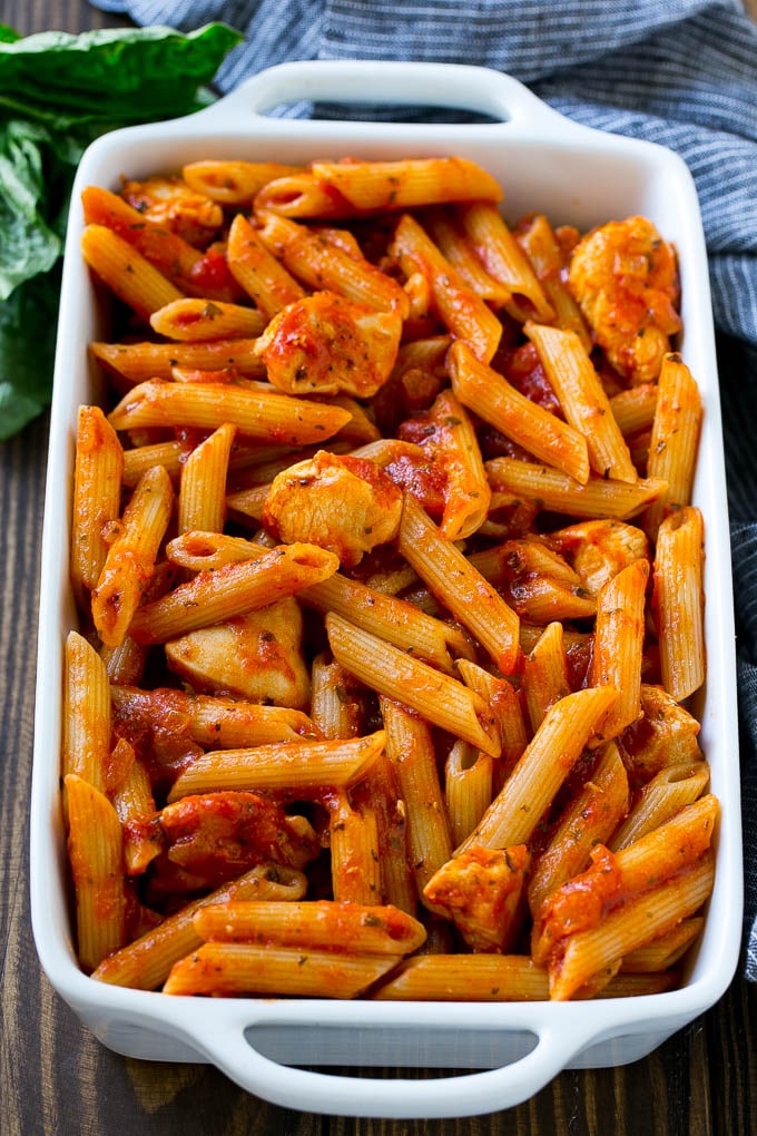 A pan of penne pasta and cooked chicken in marinara sauce.