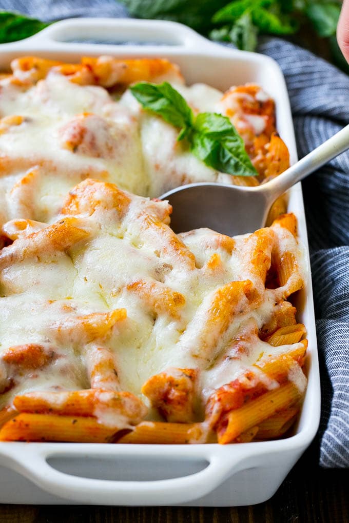 A baking dish of penne pasta with chicken, parmesan cheese and mozzarella cheese.