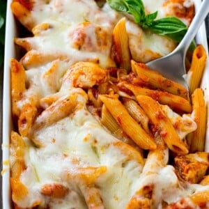 Chicken parmesan pasta in a baking dish topped with melted cheese and garnished with fresh basil.