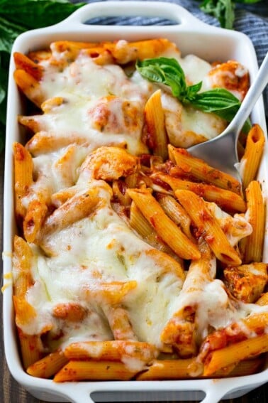 Chicken parmesan pasta in a baking dish topped with melted cheese and garnished with fresh basil.