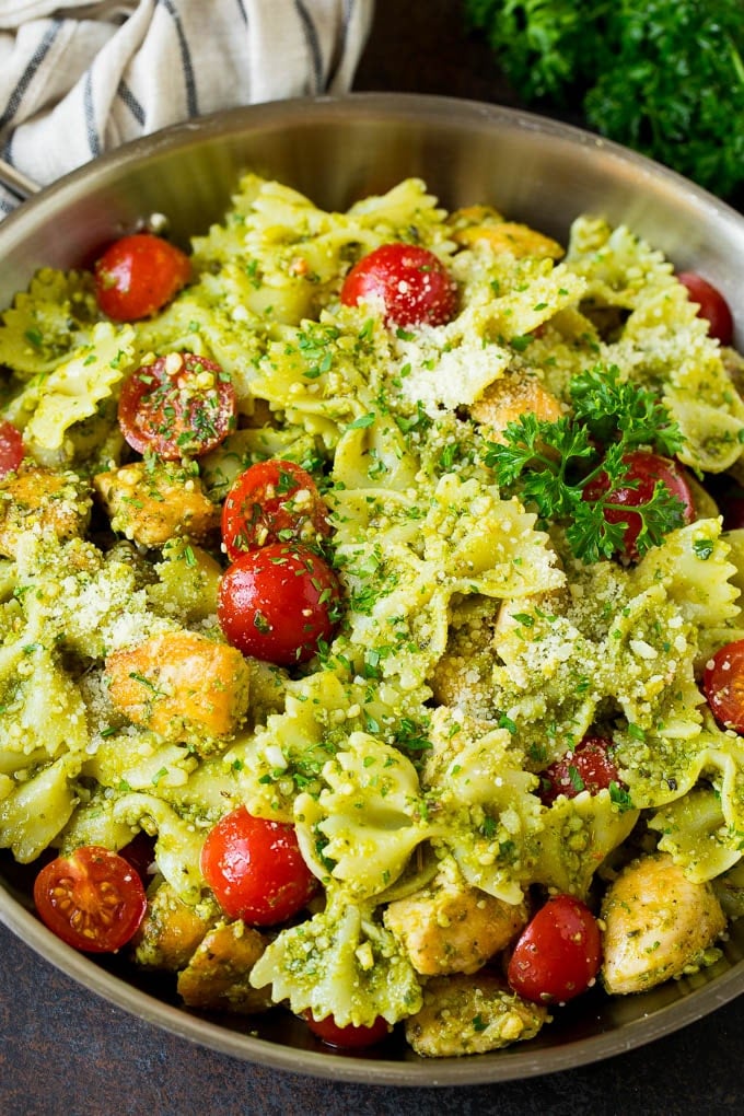 Chicken pesto pasta in a pan with cherry tomatoes and parmesan cheese.