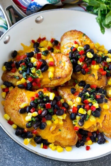 A skillet of chicken Santa Fe which is chicken breasts topped with melted cheddar, black beans, corn and red bell peppers.