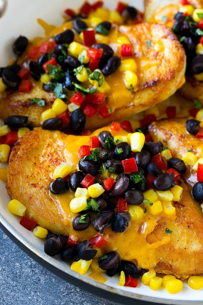 Chicken Santa Fe in a skillet topped with melted cheese, beans, corn and red peppers.