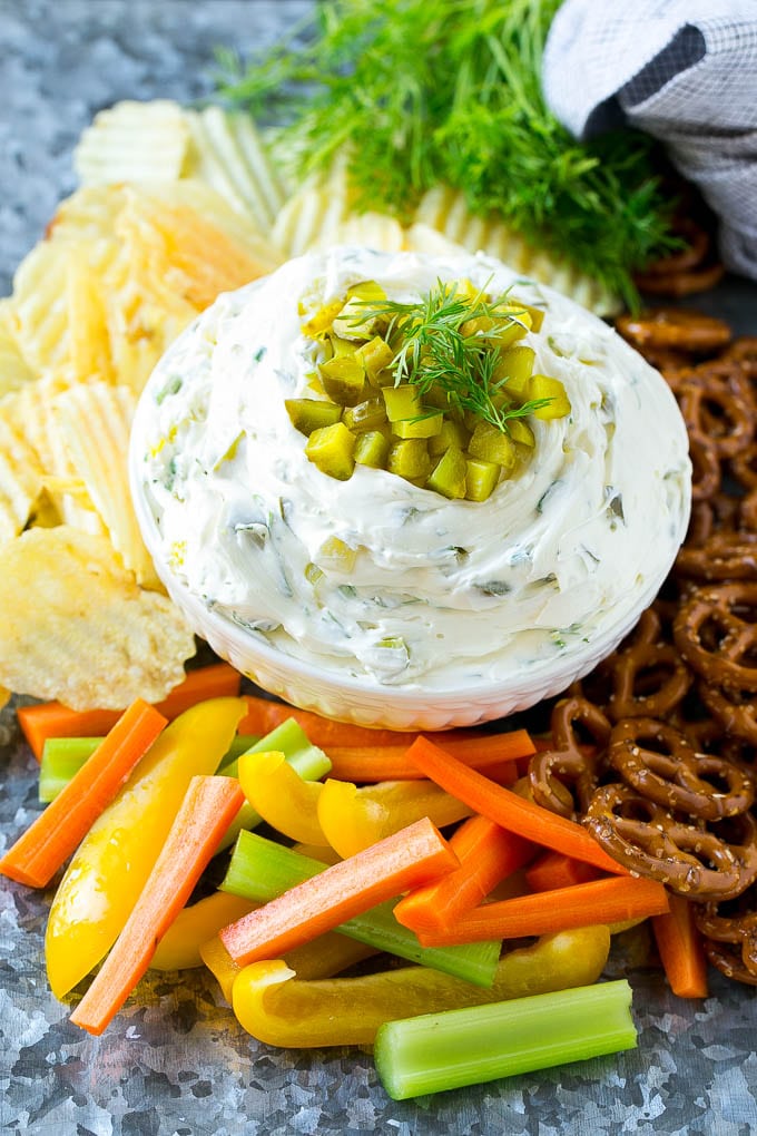 Creamy dill pickle dip with dippers such as pretzel twists, carrots and potato chips.