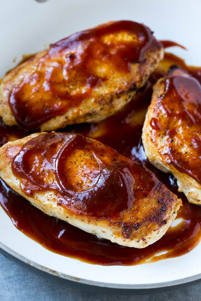 A skillet of cooked chicken breasts topped with barbecue sauce.