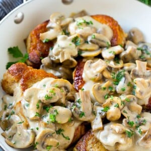 Mushroom pork chops in a skillet topped with creamy mushroom sauce and chopped parsley.