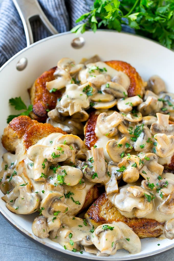 Mushroom pork chops in a skillet topped with creamy mushroom sauce and chopped parsley.