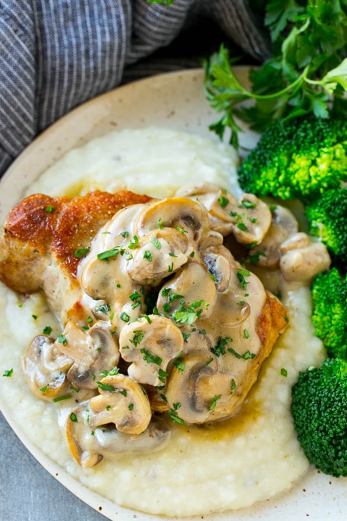 A pork chop with mushroom sauce served on mashed potatoes with a side of broccoli.