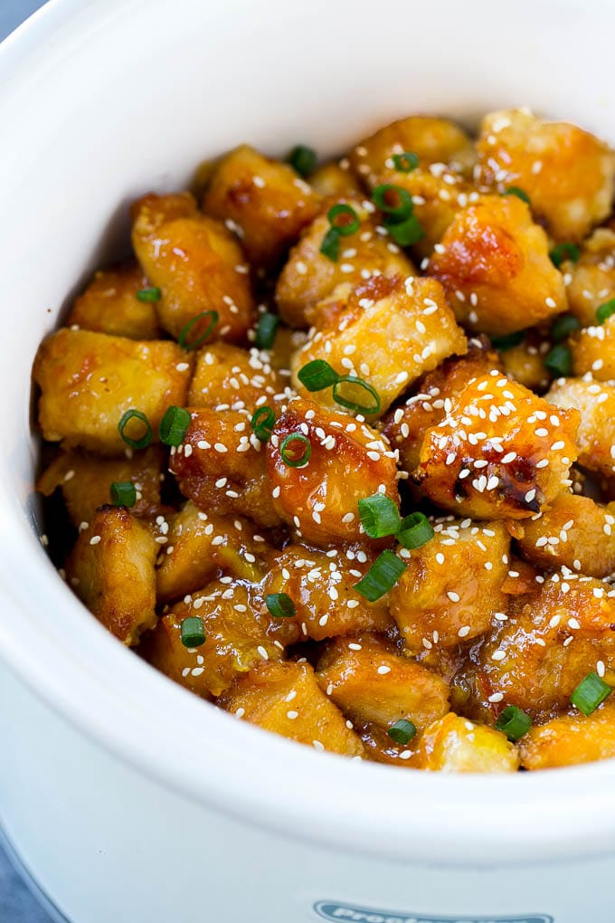 Slow cooker orange chicken inside a crock pot, topped with sesame seeds and green onions.