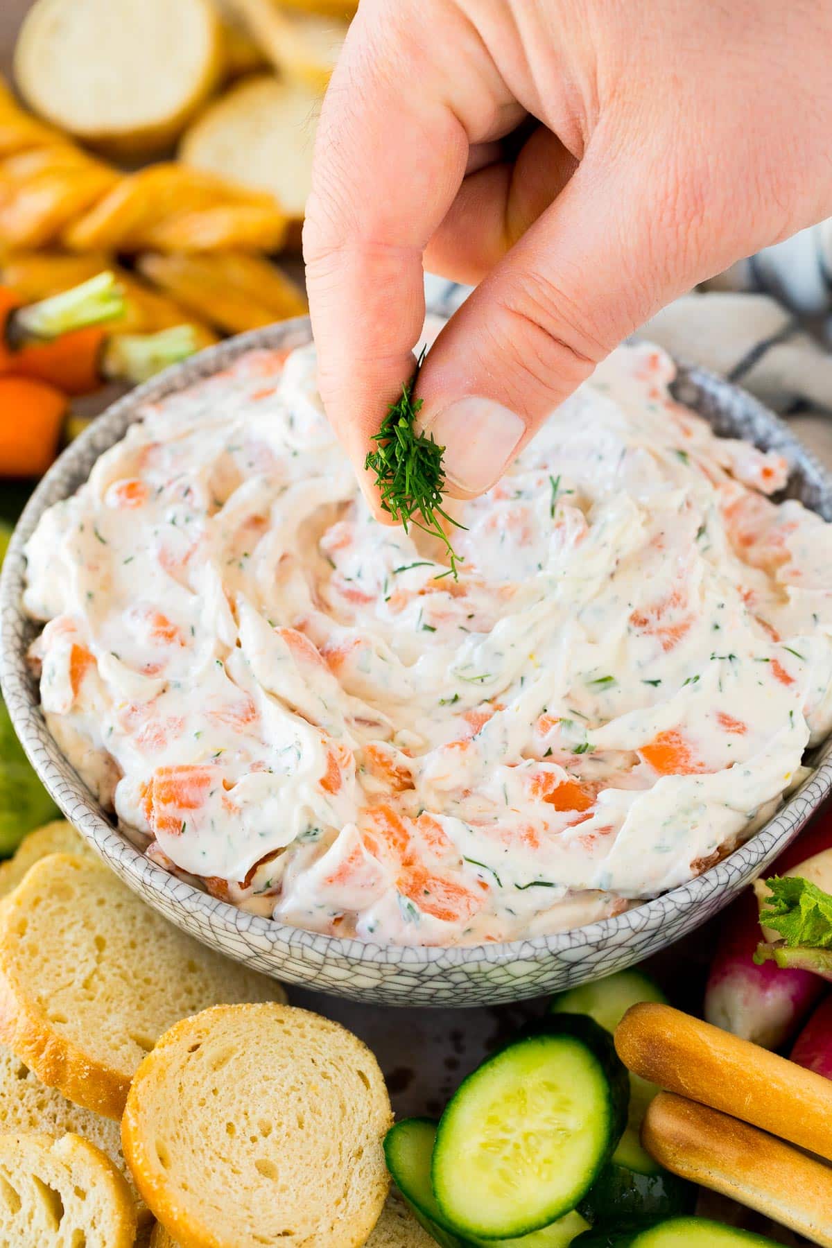 A hand garnishing the creamy appetizer with fresh dill.