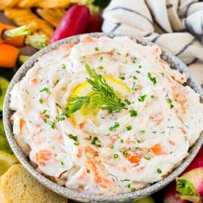 A bowl of smoked salmon dip surrounded by bread, crackers and vegetables.