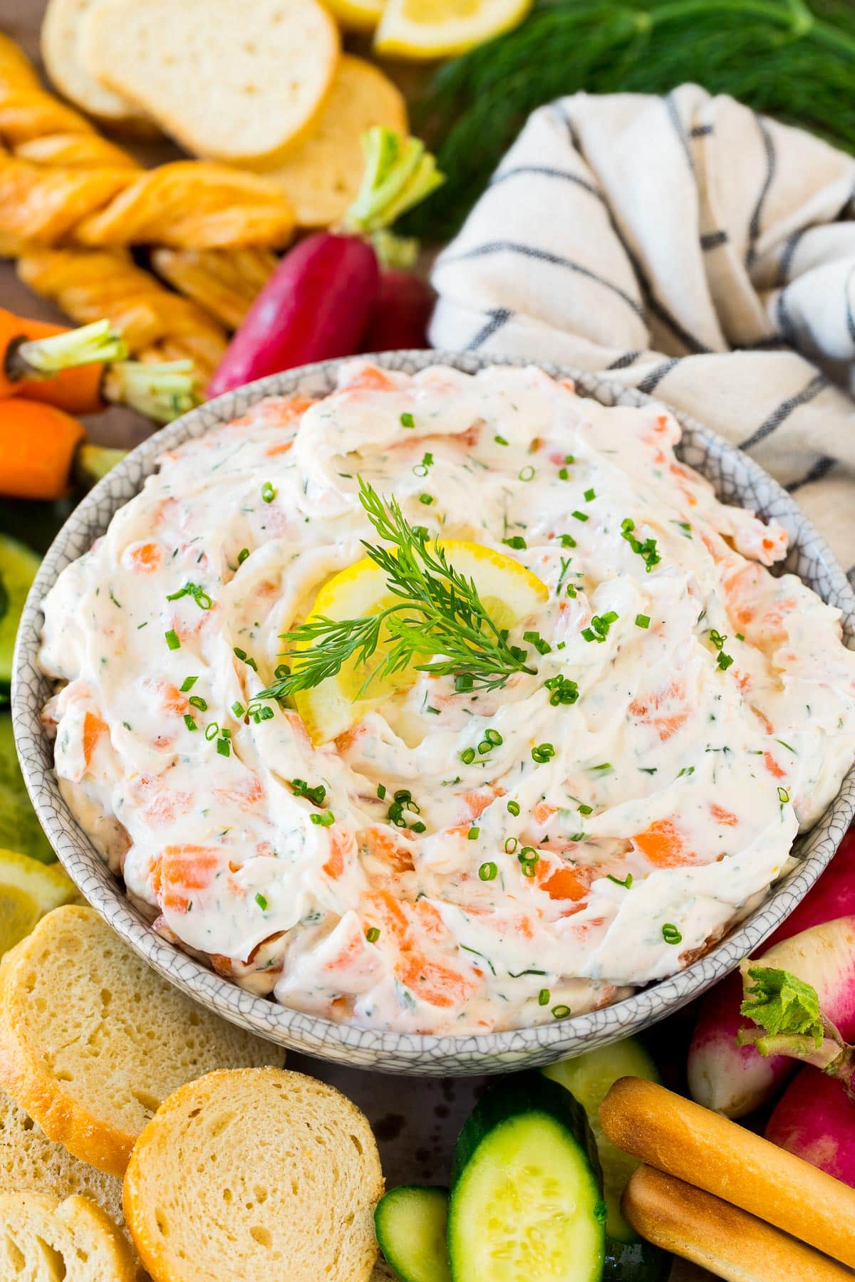 A bowl of smoked salmon dip surrounded by bread, crackers and vegetables.