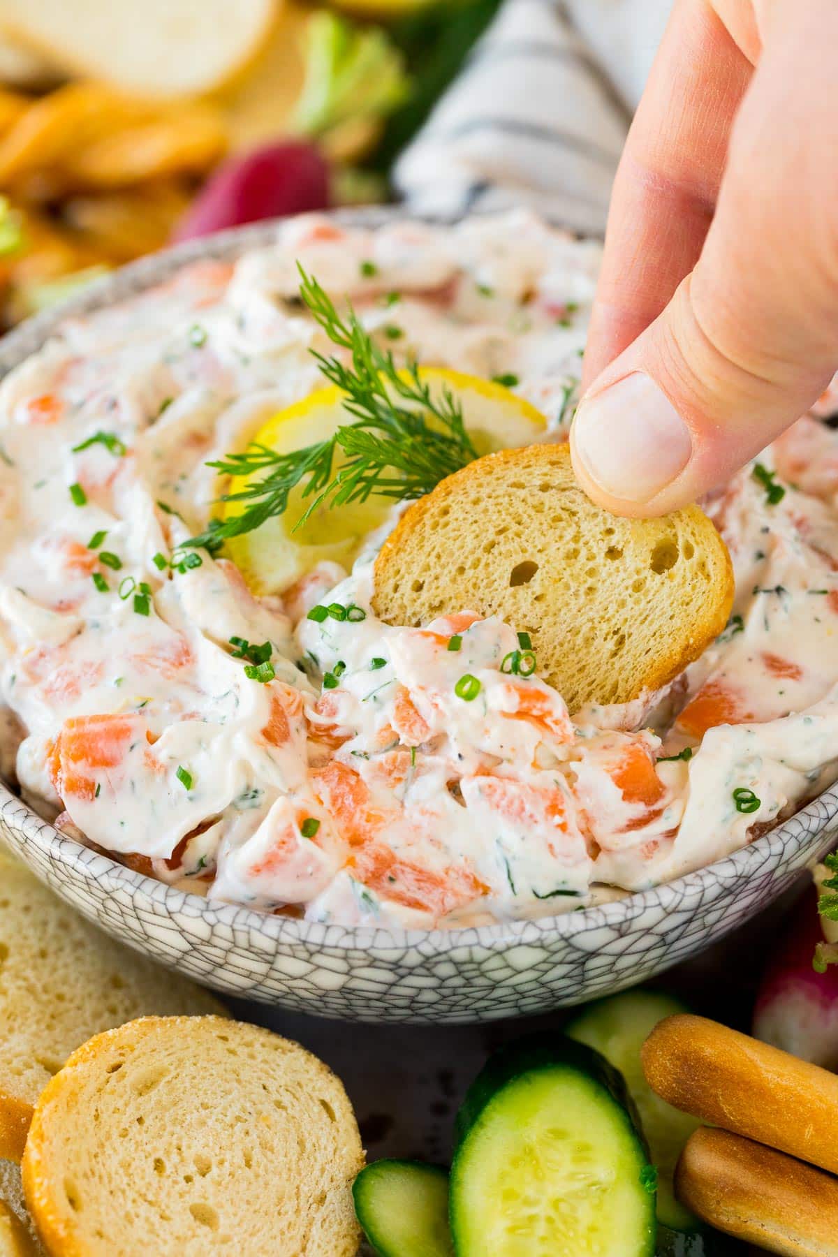 A hand scooping up a portion of salmon dip on a crostini.