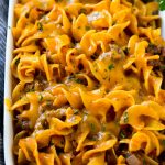 Beef noodle casserole in a serving dish topped with melted cheddar cheese and parsley.