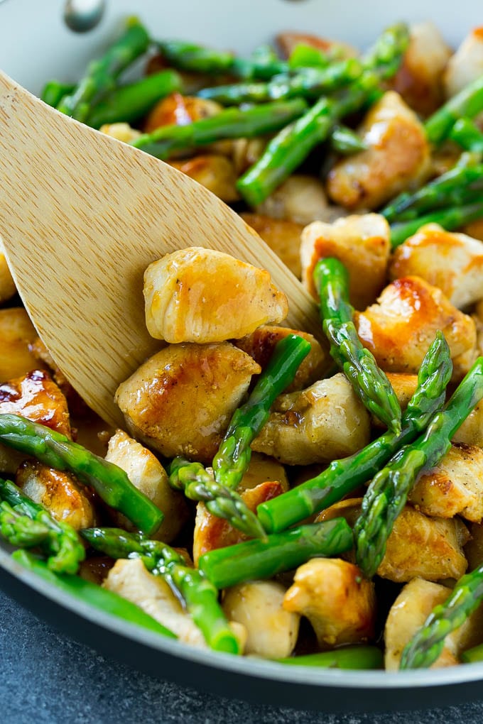 Chicken and asparagus stir fry in a skillet with a serving spatula.