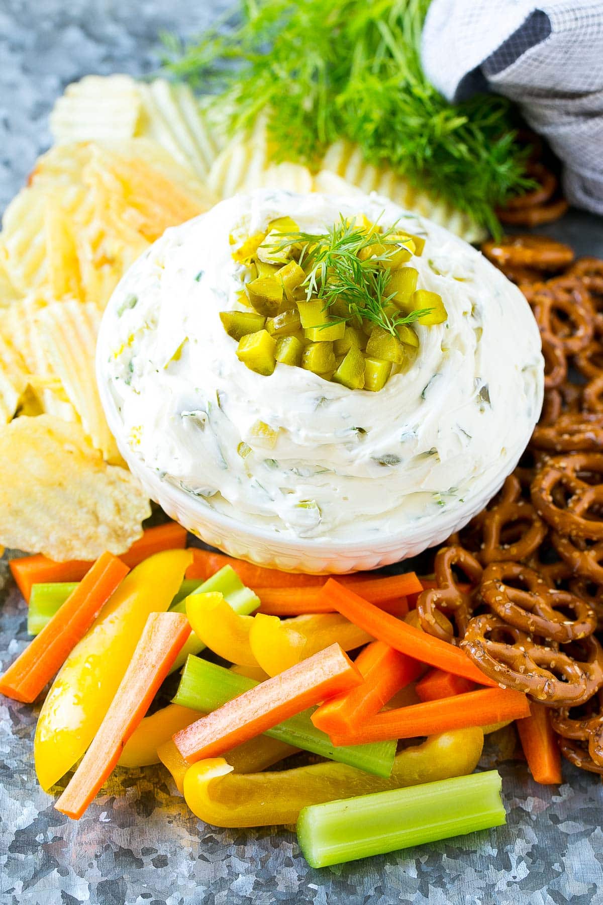 A bowl of creamy dip surrounded by vegetables, chips and pretzels.