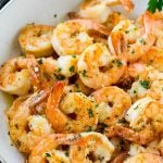 Shrimp in a skillet that are seared in garlic butter and sprinkled with parsley.