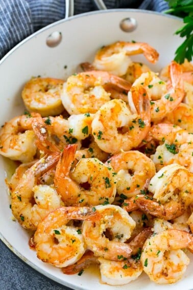 Shrimp in a skillet that are seared in garlic butter and sprinkled with parsley.