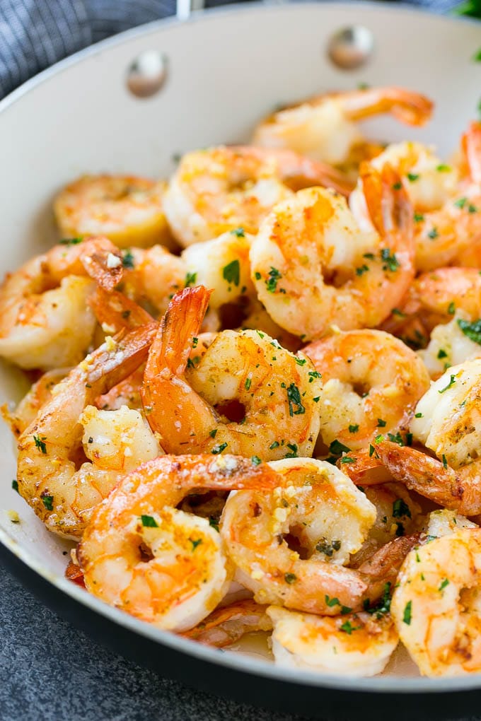 A pan of garlic butter shrimp in a savory sauce, finished off with chopped parsley.