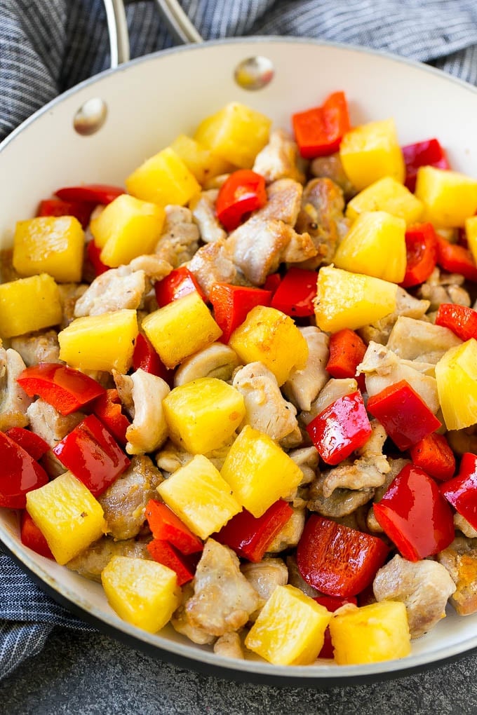 A skillet of cooked chicken, pineapple and red bell peppers.