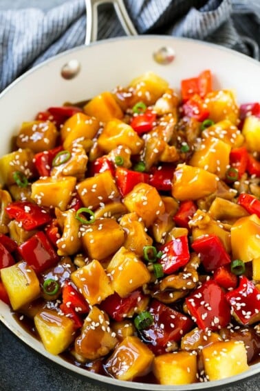Pineapple chicken stir fry in a skillet, topped with sauce, sesame seeds and green onions.