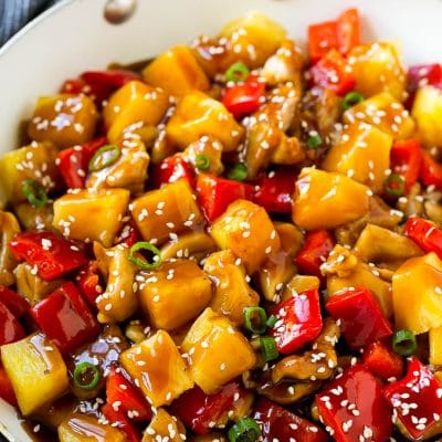 Pineapple chicken stir fry in a skillet, topped with sauce, sesame seeds and green onions.