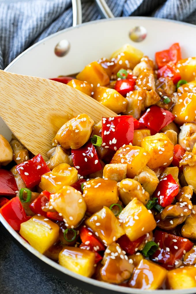 A skillet of pineapple chicken with a wooden spatula in it.