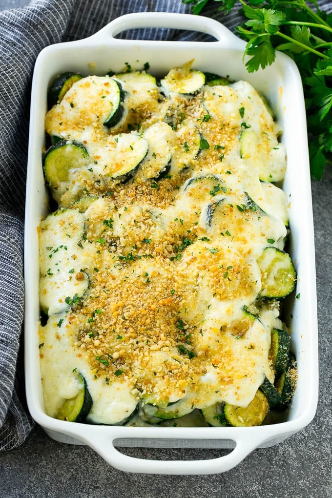 Baked zucchini gratin with layers of cheese, creamy sauce, breadcrumbs and herbs in a baking dish.
