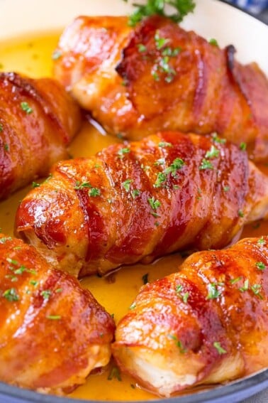 Bacon wrapped chicken breast with sauce in a skillet.
