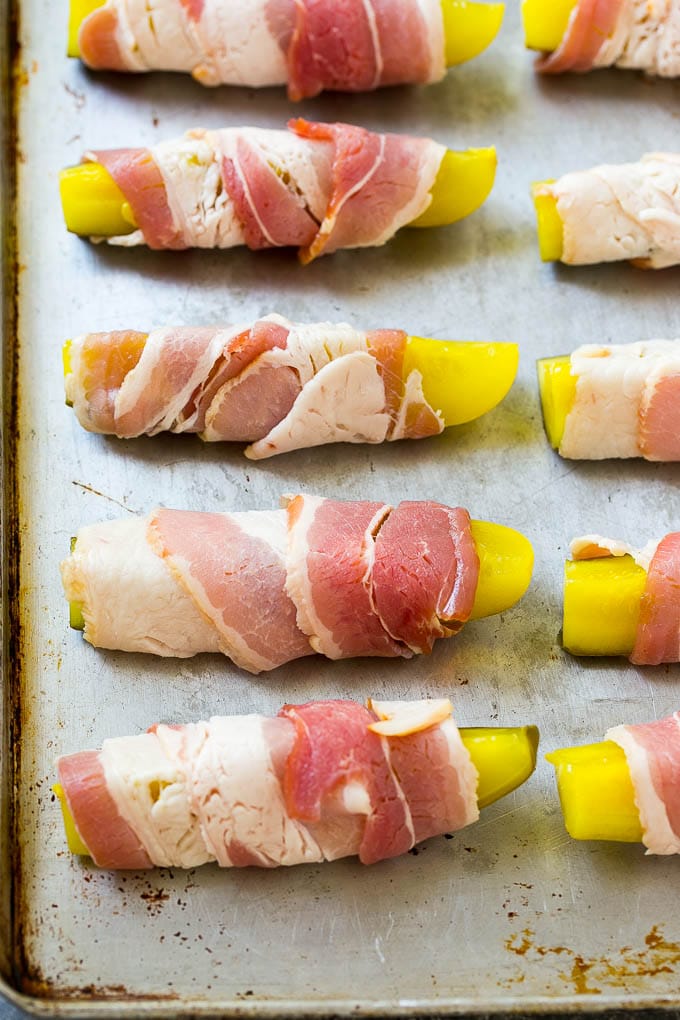 Pickle spears wrapped in bacon on a sheet pan.