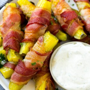 Bacon wrapped pickles on a plate with a side of ranch dressing.