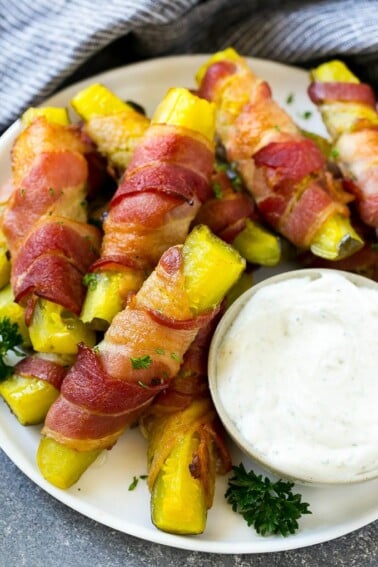 Bacon wrapped pickles on a plate with a side of ranch dressing.