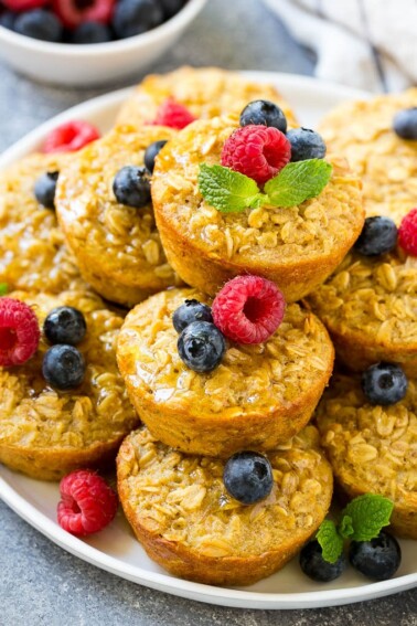 Baked oatmeal cups on a platter topped with maple syrup, berries and mint.