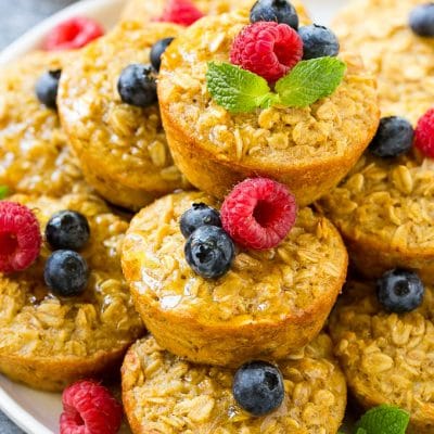 Baked oatmeal cups on a platter topped with maple syrup, berries and mint.