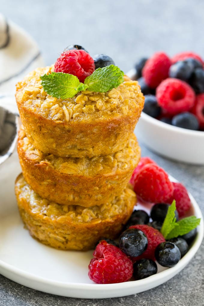 A stack of baked oatmeal cups topped with syrup, raspberries, blueberries and mint.