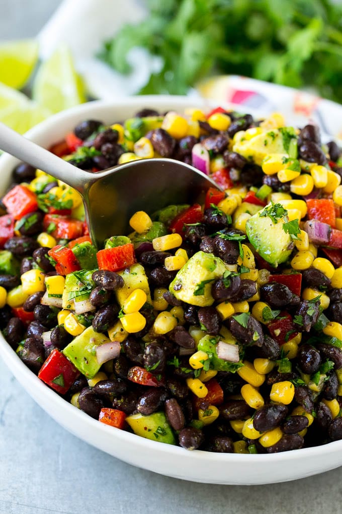 A bowl of black bean and corn salad with a serving spoon in it.