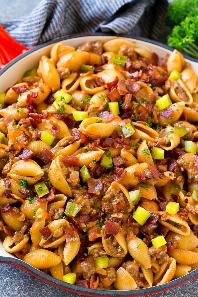 Cheeseburger pasta in a skillet topped with pickles and bacon.