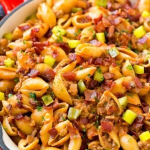 A pan of pasta with ground beef, onion, pasta shells, cheddar cheese and bacon.