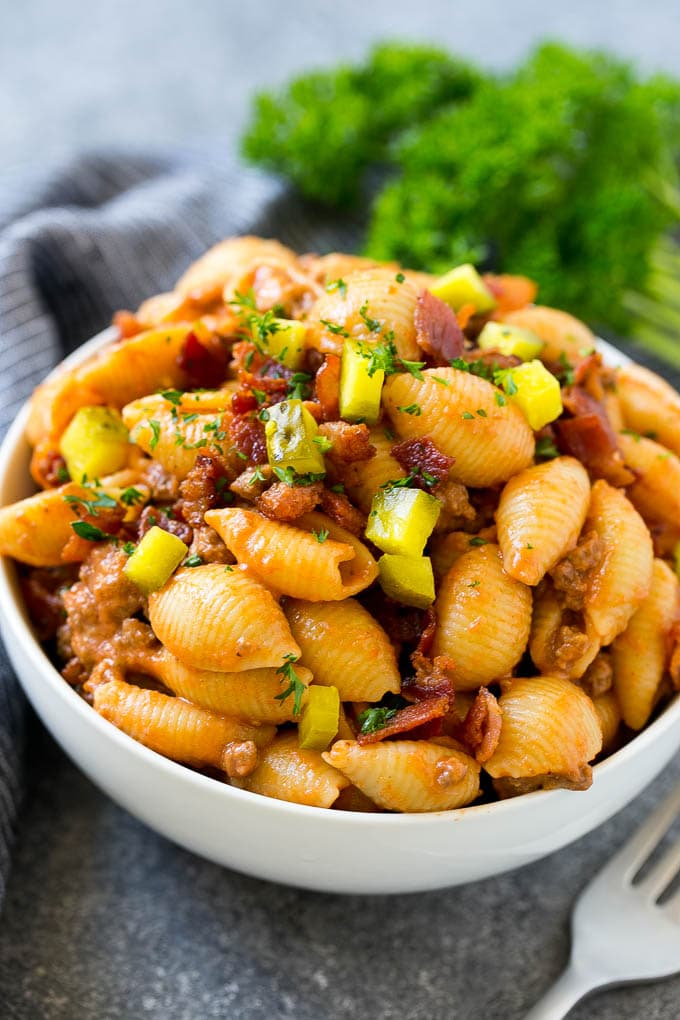 A bowl of cheeseburger pasta topped with bacon and chopped pickles.