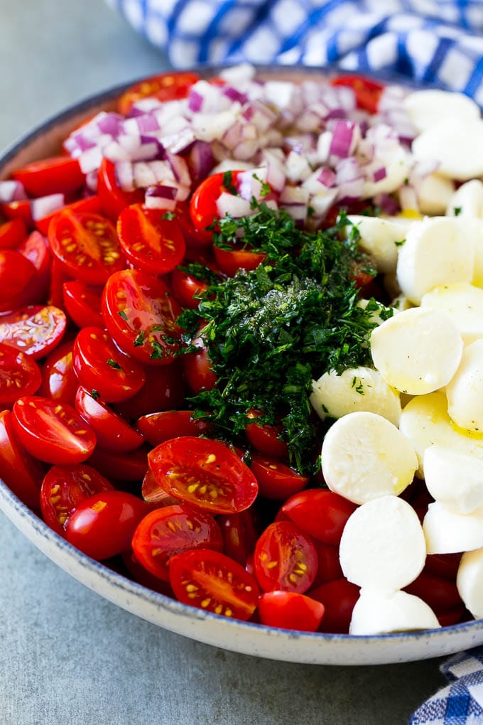 Cherry tomatoes, herbs, mozzarella balls and red onion drizzled with dressing in a bowl.