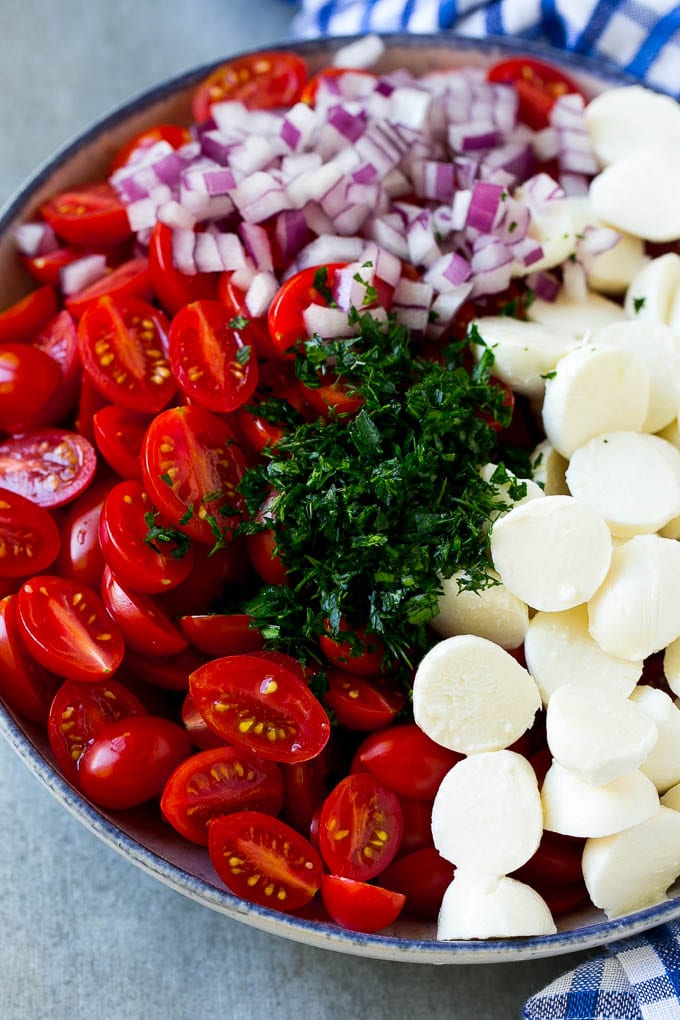 A bowl of halved cherry tomatoes, mozzarella balls, herbs and minced red onion.