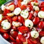 Cherry tomato salad with halved cherry tomatoes, mozzarella balls and red onion, all tossed with herbs and dressing.
