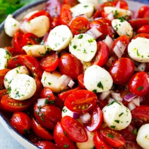 Cherry tomato salad with halved cherry tomatoes, mozzarella balls and red onion, all tossed with herbs and dressing.
